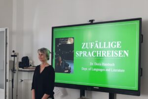 Prof. Dr. Doris Hambuch vor der Präsentationsfolie „Zufällige Sprachreisen“
